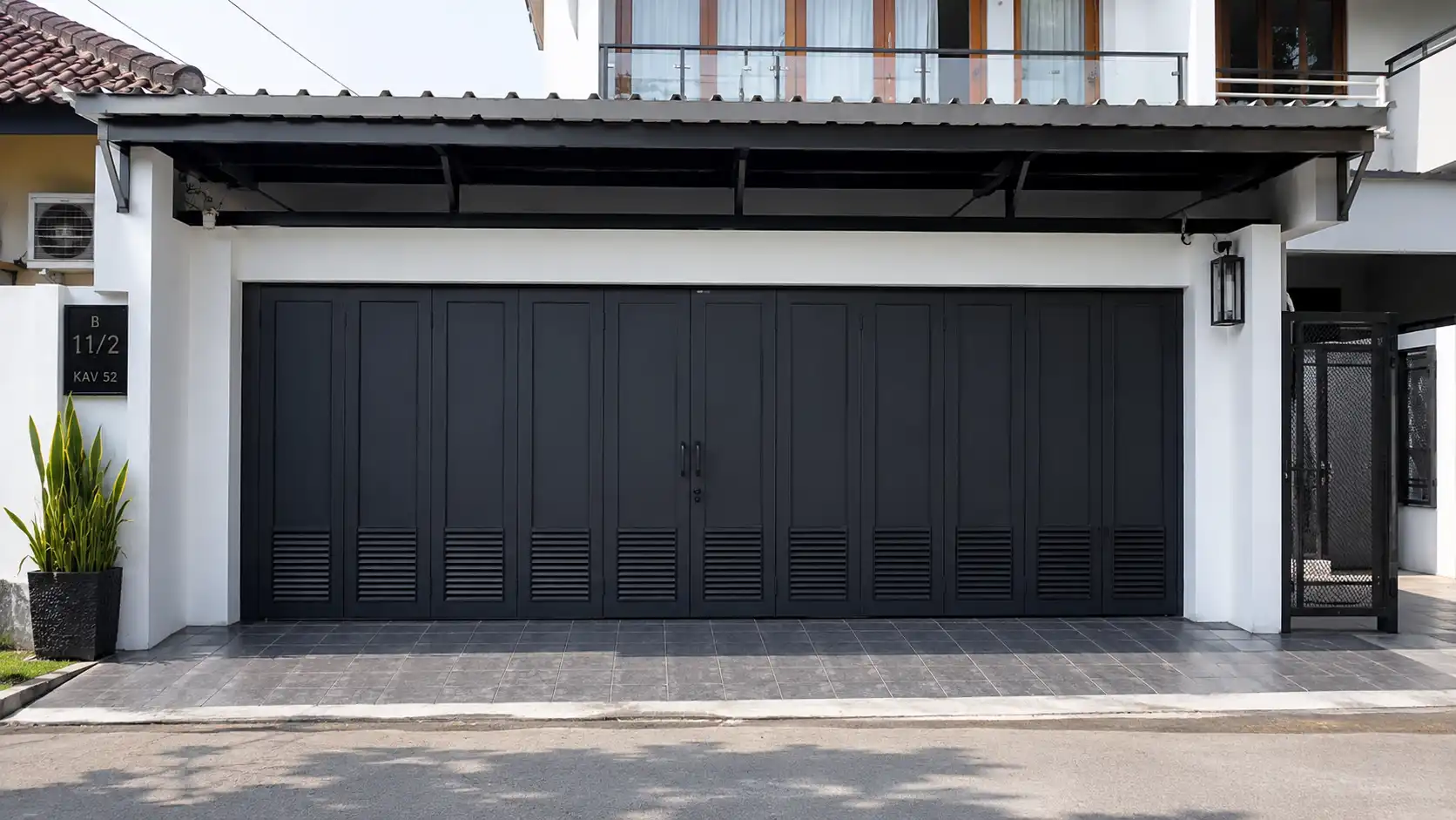 Pintu lipat besi minimalis pada garasi rumah modern dengan fasad rapi dan pencahayaan natural.